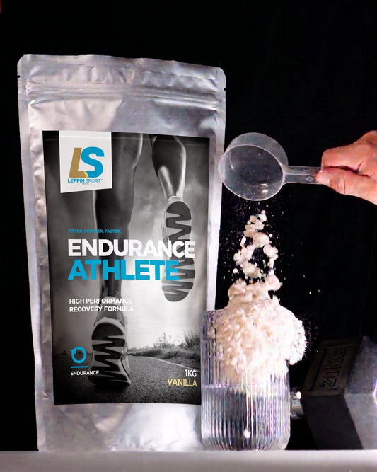 A silver stand-up pouch of Endurance Athlete powder by LSF Nutrition is shown next to a clear scoop pouring white powder into a ribbed glass against a black background.