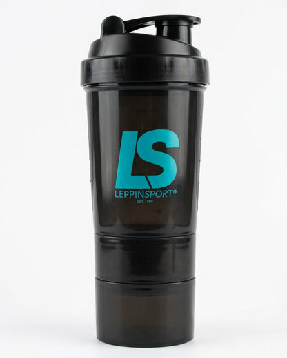 A close-up lifestyle shot of a person holding a black shaker bottle with a teal 'LS' logo on a red running track. The person is wearing white athletic socks with a matching teal and blue 'LS' logo.
