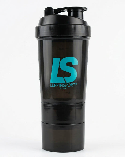 A close-up lifestyle shot of a person holding a black shaker bottle with a teal 'LS' logo on a red running track. The person is wearing white athletic socks with a matching teal and blue 'LS' logo.